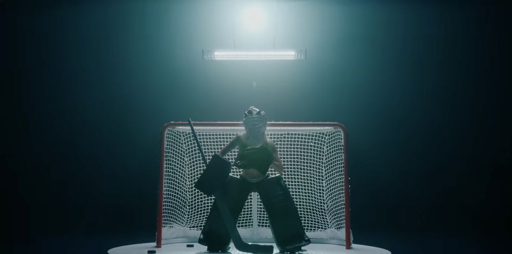 Sydney Sweeney in hockey goalkeeping equipment in front of a goal in the Novig campaign film.
