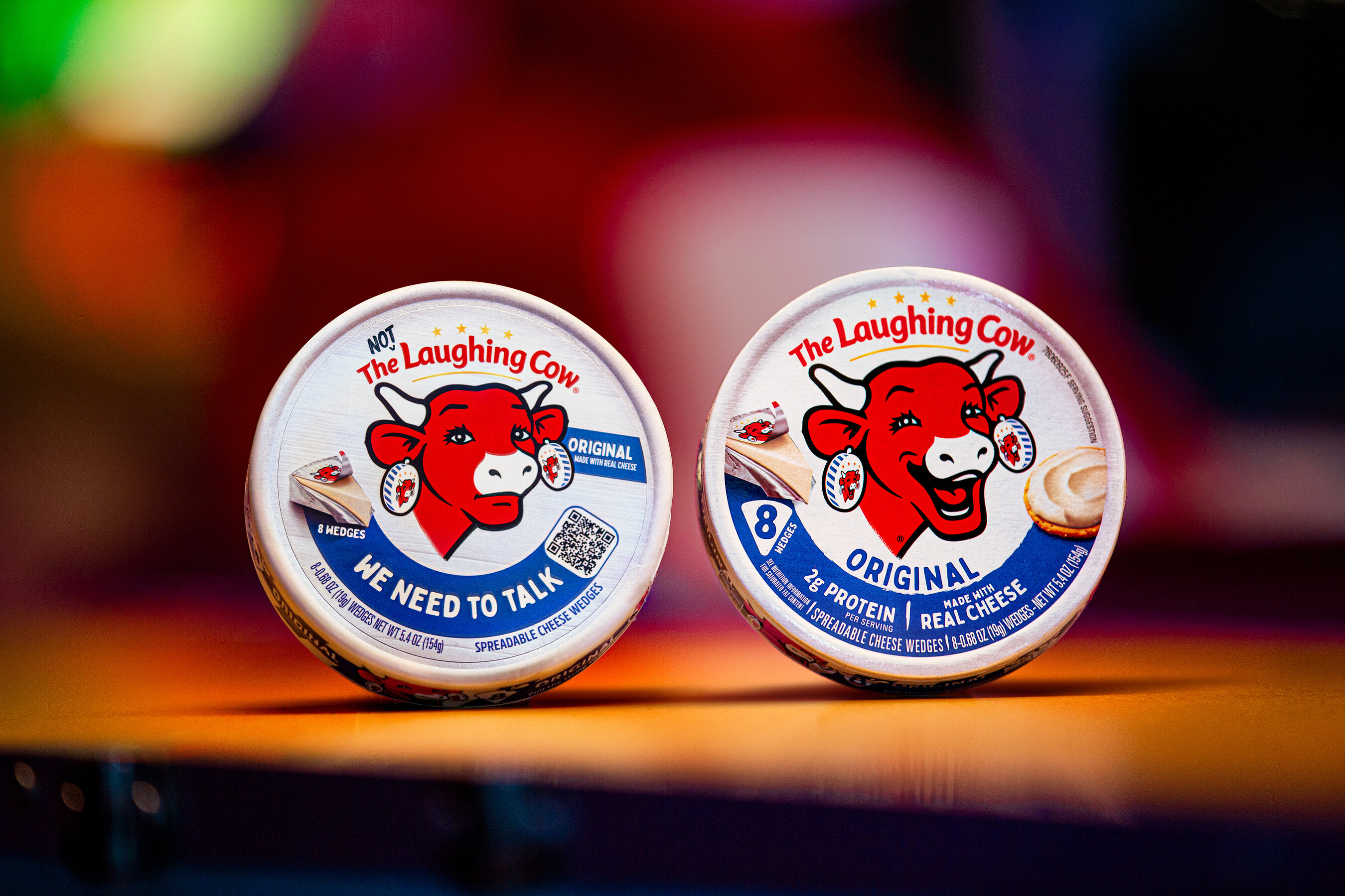 Two original Laughing Cow packs side by side: a temporarily unsmiling red cow on the left and the familiar smiling cow on the right.